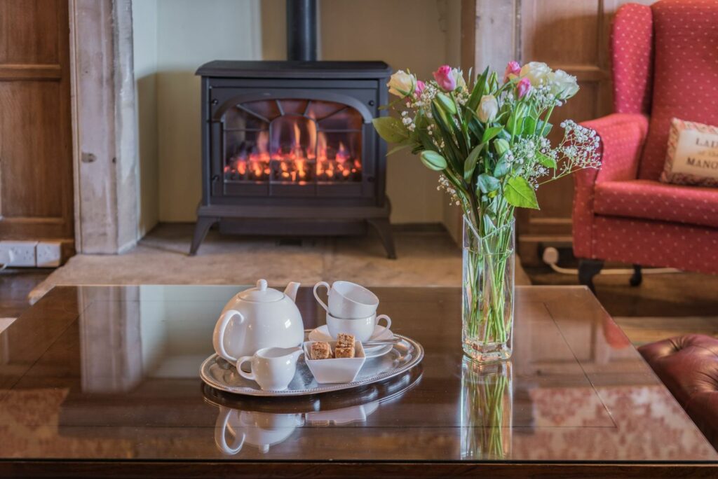 Tea set and vase with flowers on a table in front of a fireplace. 