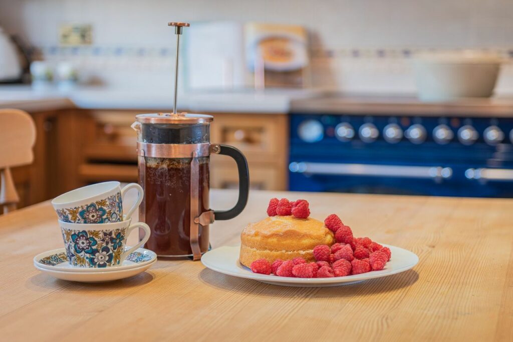 French press, two cups and desserts on a table. 