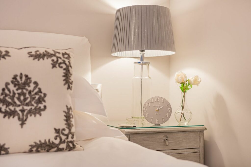 Nightstand with clock and a vase with white roses on it. 