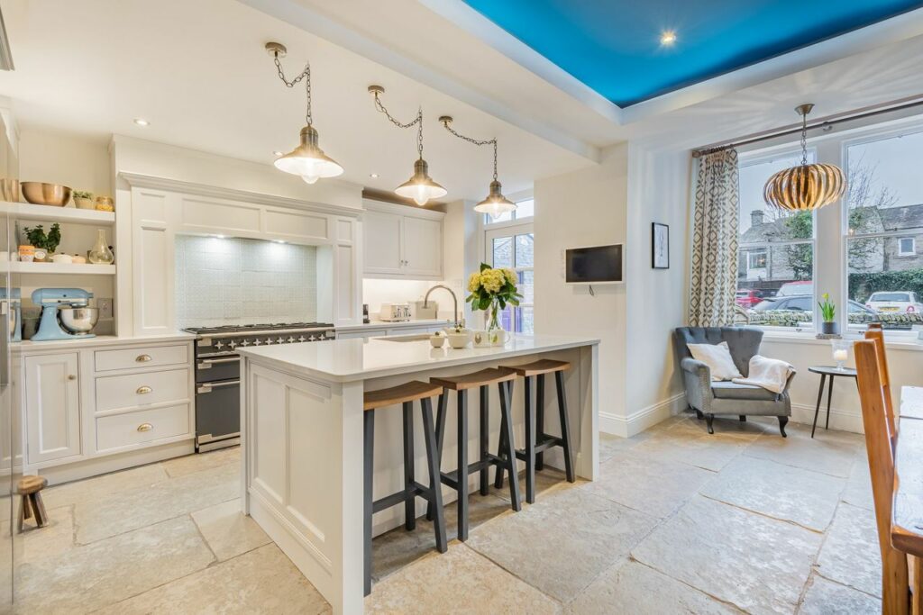 Wide, white kitchen with stone floor. 