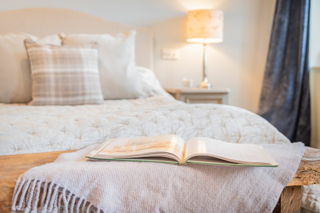 Open book on a bench in front of a bed.