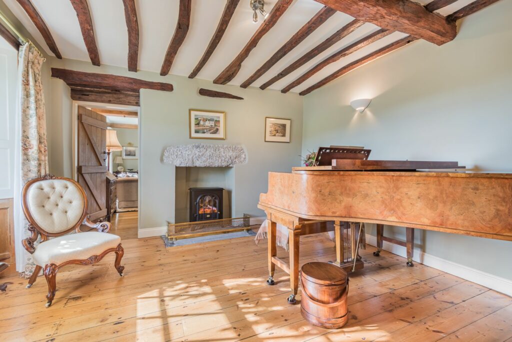 Spacious room in farm style interior, with piano and a chair. 