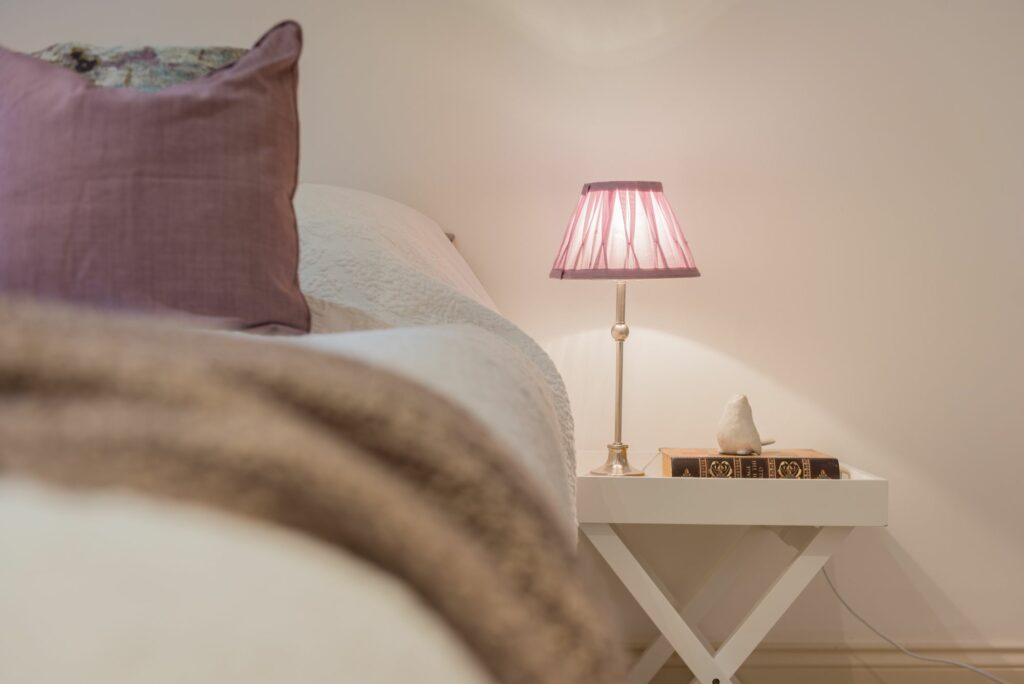 Bed beside a nightstand with a lamp and a book on it. 