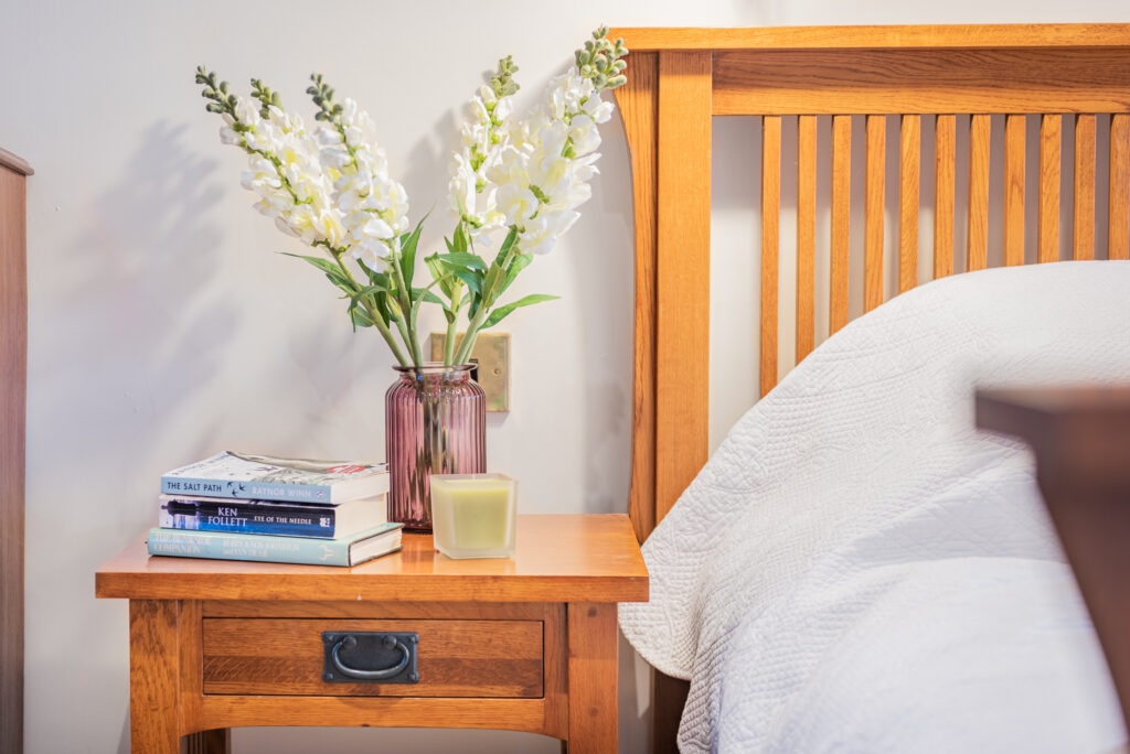 Bed, night stand with flower and books on it. 