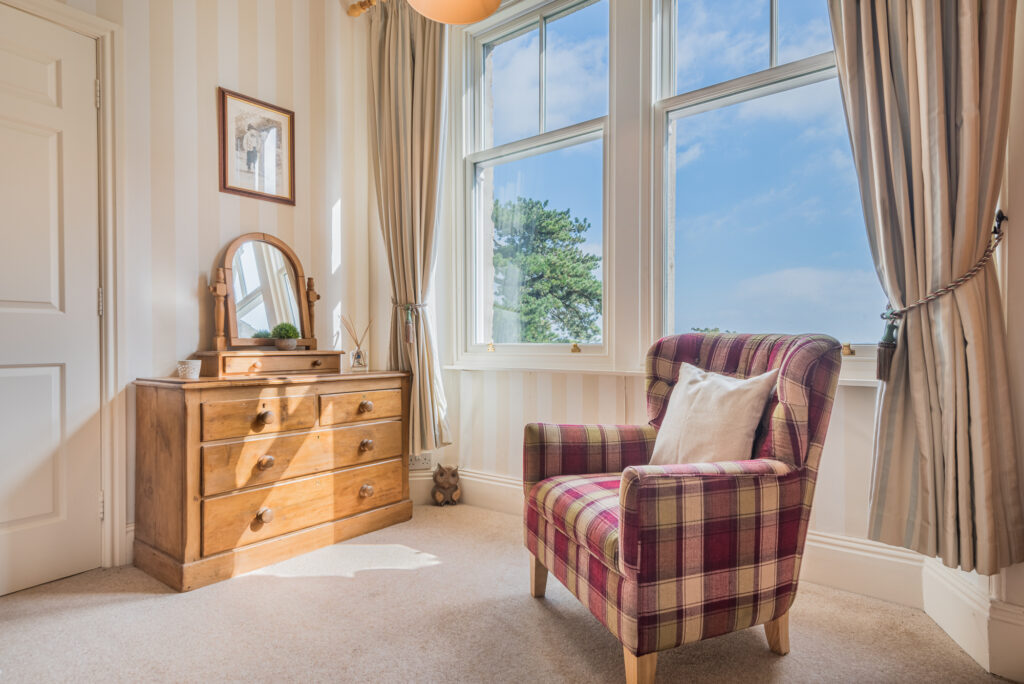 Corner of a room with big window, armchair and dressing table. 