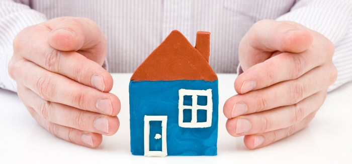 Man holding his hands over a small house 