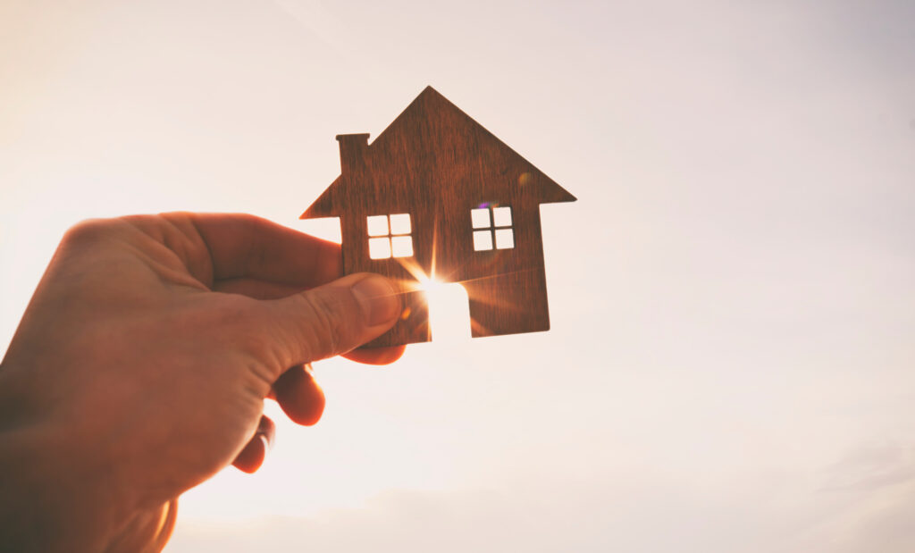 Hand holds a little house figure against the sun. 