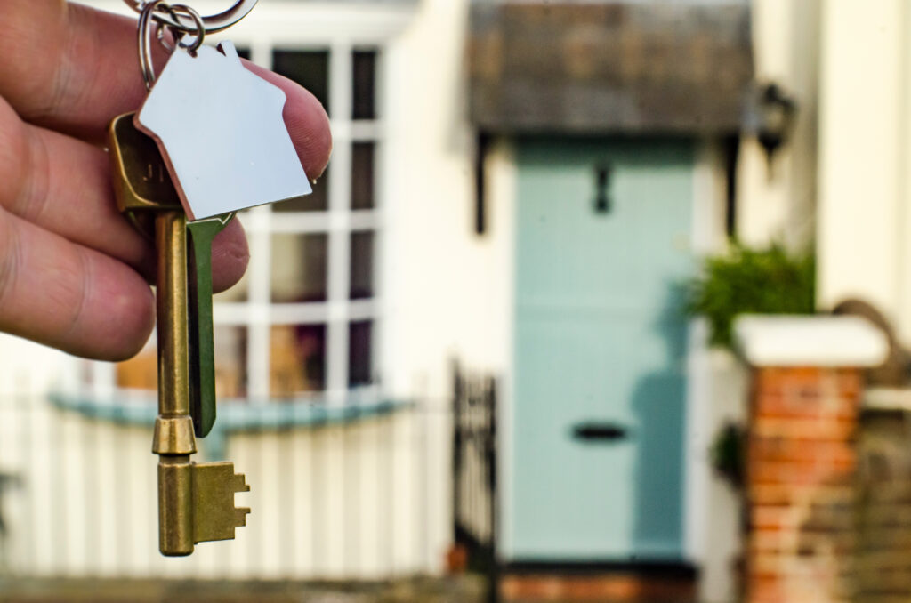 Person holding a set of keys in front of a house.