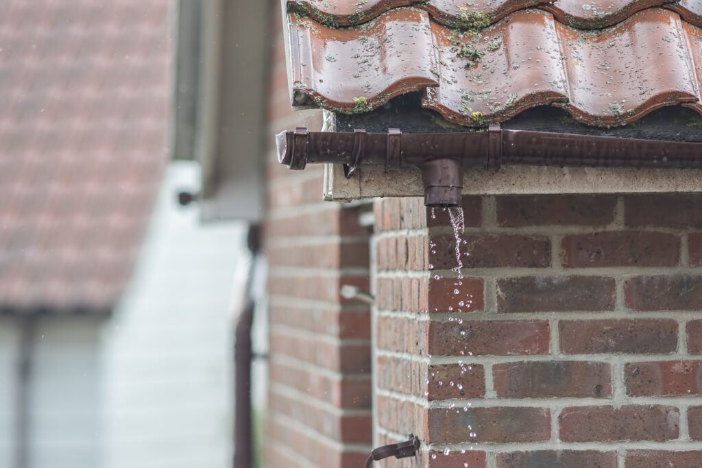 Broken gutter missing a downpipe. House guttering repair leaking rain water. Drainage problem with brown UPVC pipe.