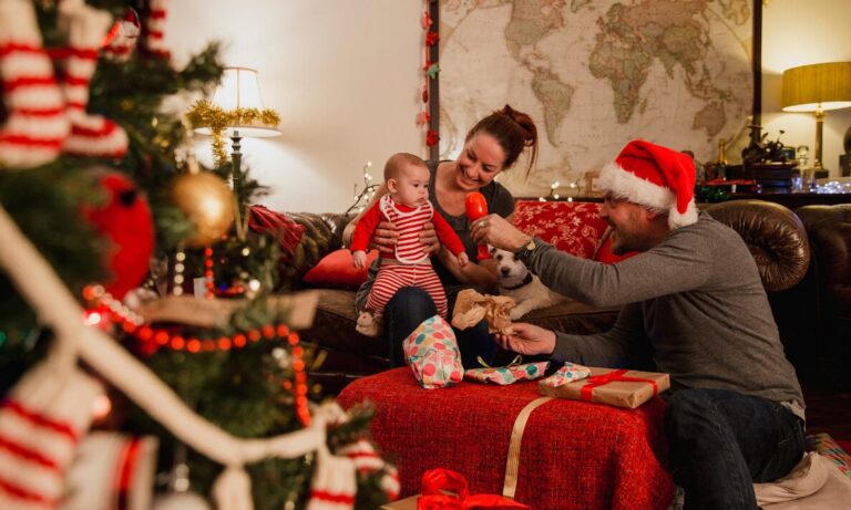 A family sitting together opening Christmas presents by the tree with festive decorations and a cosy living room background.
