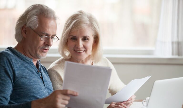 Older couple reviewing rental documents together at a table, representing landlords assessing property paperwork and income security.