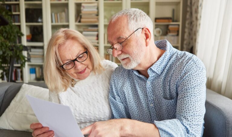 Older couple sitting on a sofa reviewing a rent related document together, representing landlords and tenants adapting to Section 13 rent review changes.