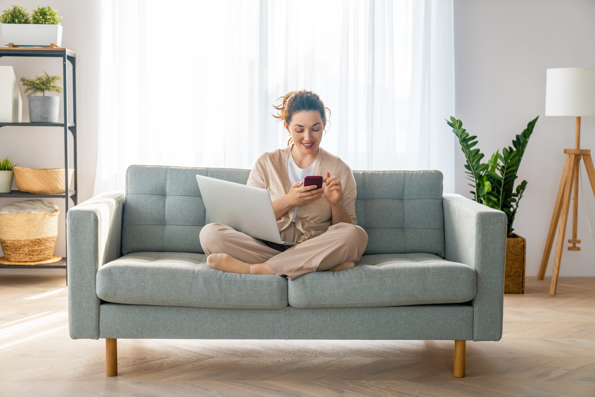 Woman sitting on a sofa using a laptop and phone, reflecting first-time buyer research and planning a property purchase in Bristol.