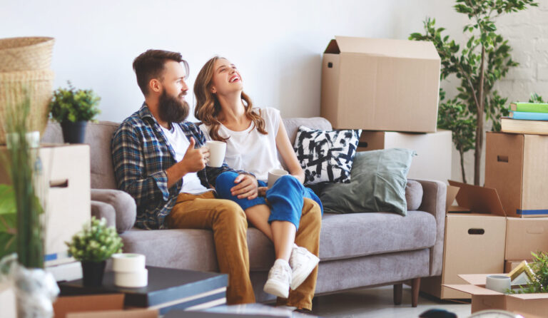 Couple relaxing in a living room surrounded by moving boxes after switching to a long-term rental property.
