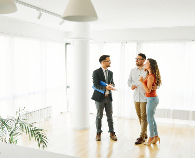 Real estate agent holding a blue folder while showing a bright, modern home to a smiling couple.
